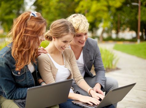 summer, education, technology and people concept - group of students or teenagers with laptop computers sitting on bench outdoors