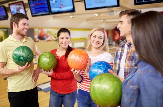 people, leisure, sport, friendship and entertainment concept - happy friends holding balls and talking in bowling club