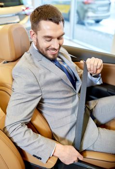 auto business, car sale, consumerism, technology and people concept - happy man sitting in car with smartphone at auto show or salon