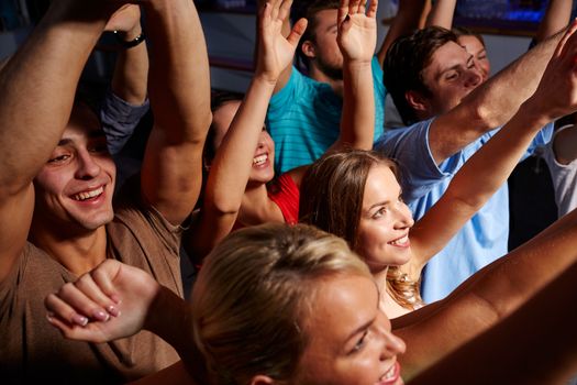 party, holidays, celebration, nightlife and people concept - group of smiling friends waving hands at concert in club