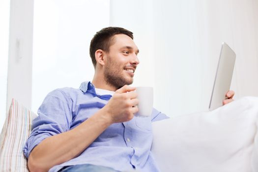 technology, people and leisure concept - handsome man with tablet pc computer and cup drinking coffee or tea at home