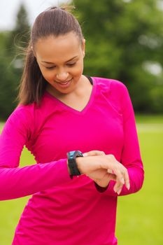 sport, fitness, technology, healthcare and people concept - smiling young woman with heart rate watch outdoors