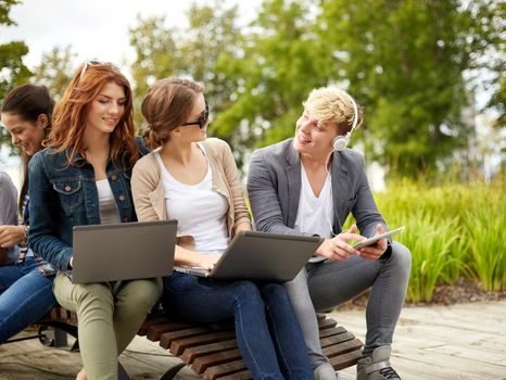 summer, education, technology and people concept - group of students or teenagers with laptop computers sitting on bench outdoors