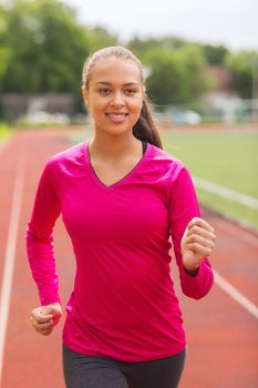 fitness, sport, training and lifestyle concept - smiling african american woman running on track outdoors