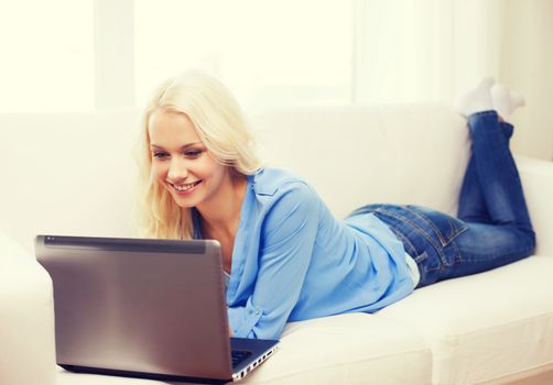 home, technology and internet concept - smiling woman lying on the couch with laptop computer at home