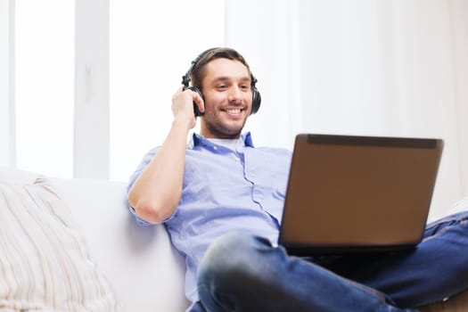 technology, home, music and lifestyle concept - smiling man with laptop and headphones at home