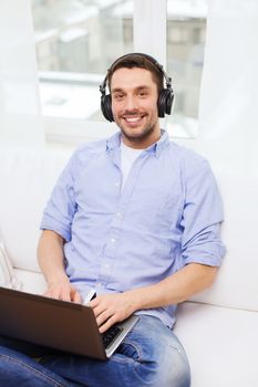 technology, home, music and lifestyle concept - smiling man with laptop and headphones at home