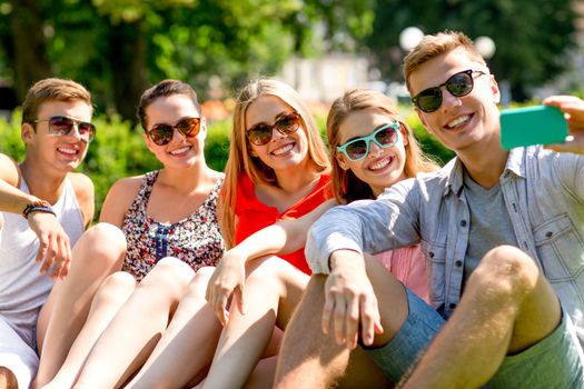 friendship, leisure, summer, technology and people concept - group of smiling friends with smartphone making selfie in park