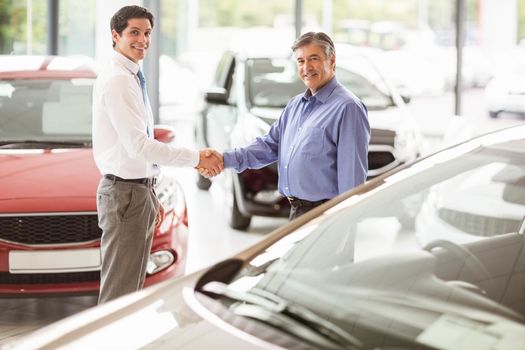 Businessman shaking a customer hand at new car showroom