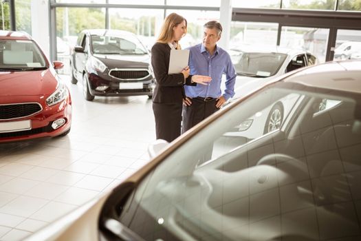 Businesswoman and her client looking at a car at new car showroom