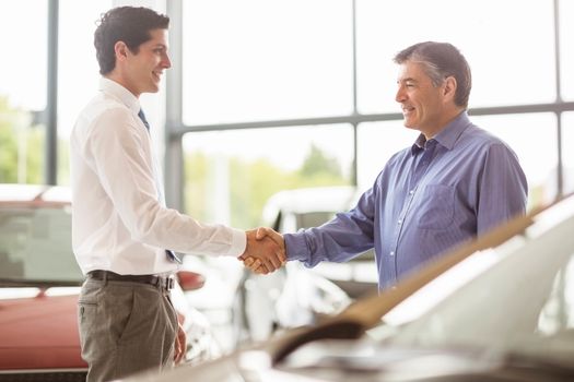 Businessman shaking a customer hand at new car showroom