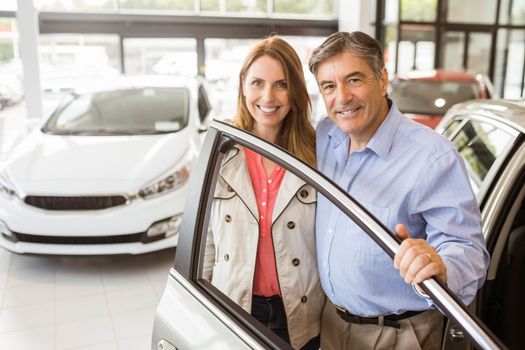 Smiling couple leaning on car at news car showroom