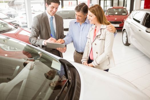 Smiling businessman presenting a car at new car showroom