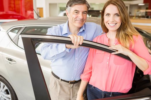 Smiling couple leaning on car at news car showroom