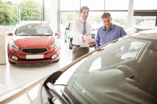 Salesman showing somethings to a man at new car showroom