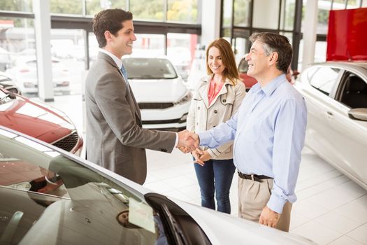 Smiling businessman presenting a car at new car showroom