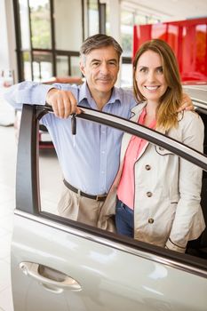 Smiling couple leaning on car at news car showroom