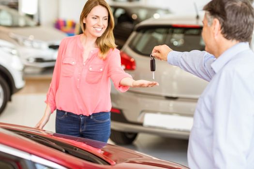 Smiling businessman giving car key to happy customer at new car showroom