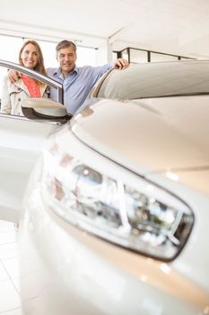 Smiling couple leaning on car at news car showroom