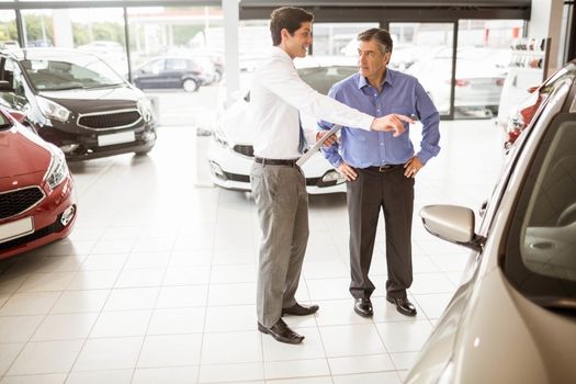 Salesman showing somethings to a man at new car showroom