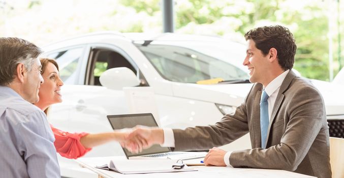 Smiling couple buying a new car at new car showroom