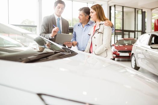 Smiling businessman presenting a car at new car showroom