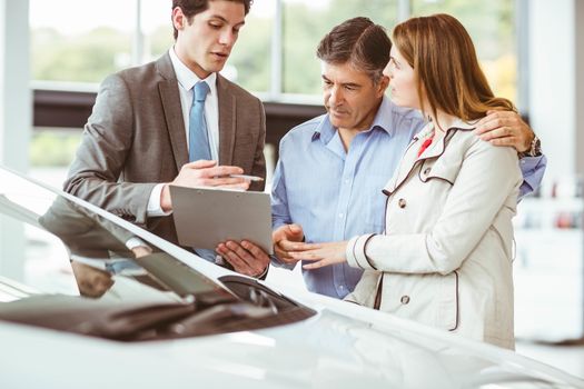 Smiling businessman presenting a car at new car showroom