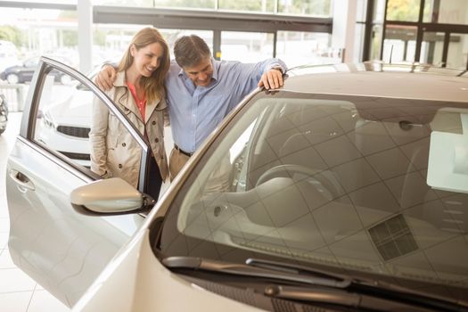 Smiling couple leaning on car at news car showroom