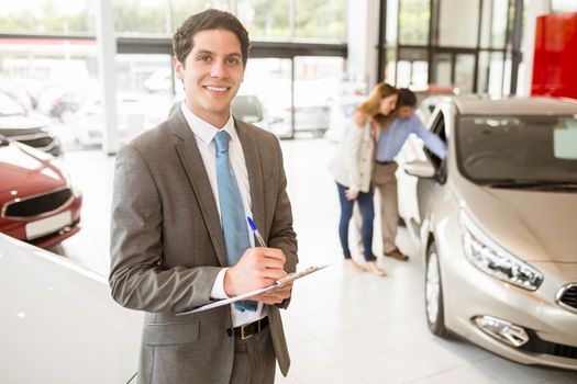 Smiling businessman writing on his clipboard at new car showroom