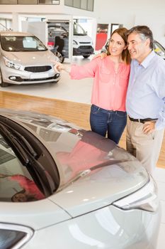 Couple talking together while looking at car at new car showroom