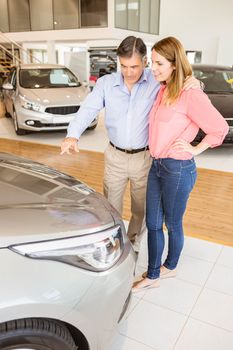 Couple talking together while looking at car at new car showroom