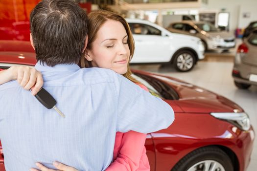 Smiling woman holding key while hugging her husband at new car showroom
