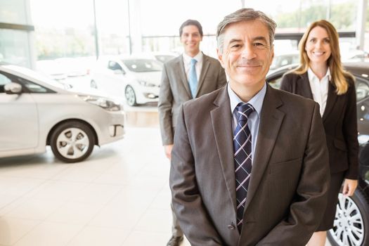 Group of smiling business team standing together at new car showroom