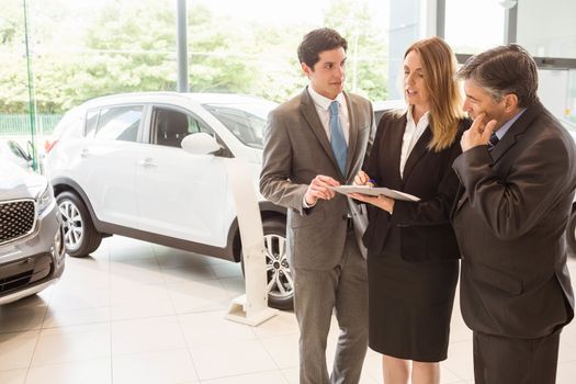 Sales team look at a clipboard at new car showroom