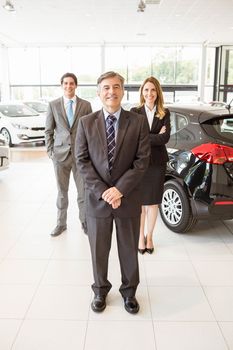 Group of smiling business team standing together at new car showroom