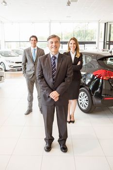 Group of smiling business team standing together at new car showroom