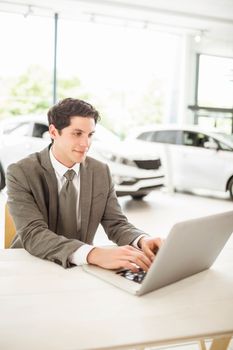 Smiling salesman behind his desk at new car showroom