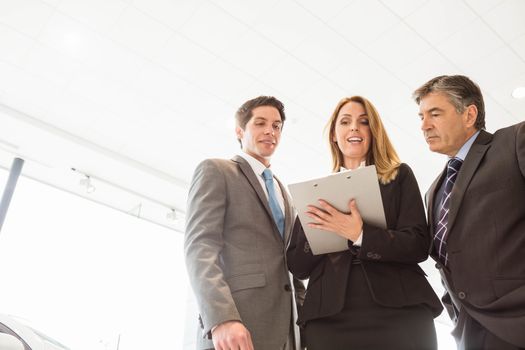 Group of smiling business team standing together at new car showroom