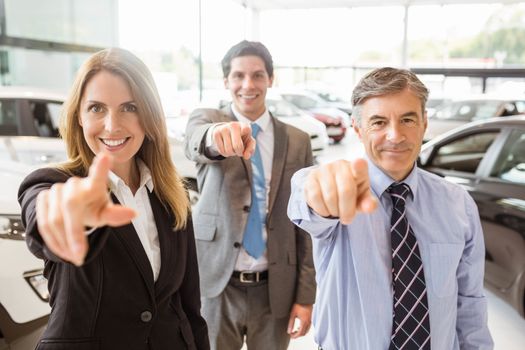 Group of smiling business team pointing together at new car showroom