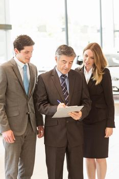 Group of smiling business team standing together at new car showroom