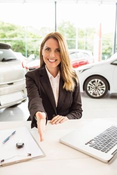 Smiling saleswoman ready to shake hand at new car showroom
