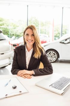 Smiling saleswoman behind her desk at new car showroom