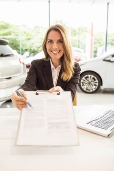 Smiling saleswoman holding a clipboard at new car showroom