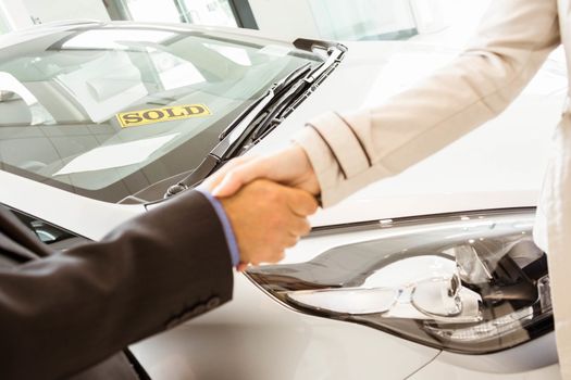 Salesman shaking a customer hand at new car showroom