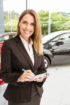 Smiling saleswoman checking a car at new car showroom