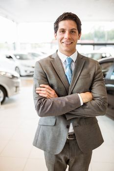 Smiling businessman standing with arms crossed at new car showroom