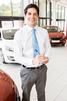 Smiling businessman writing on clipboard at new car showroom