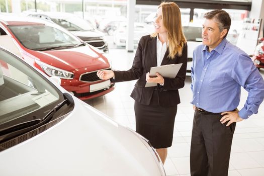 Smiling businesswoman showing car to customer at new car showrom