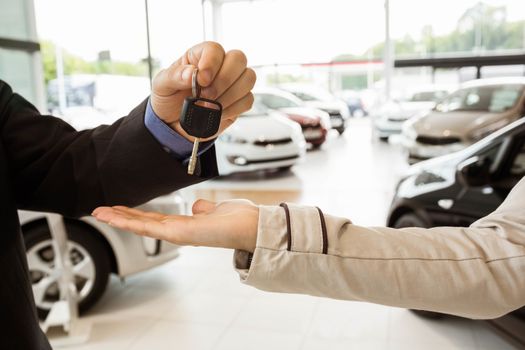 Salesman offering car key to a customers at new car showroom