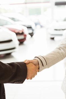 Salesman shaking a customer hand at new car showroom